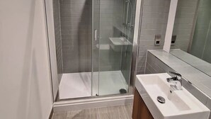 A modern bathroom with a glass-enclosed shower, a wooden vanity with a white sink, and grey tiled walls.