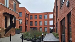 A courtyard with brick buildings, a central pathway, and a small garden area.