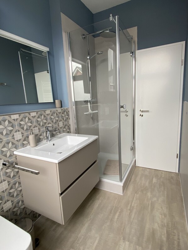 A modern bathroom with a glass-enclosed shower, a white sink, and a mirror above it. - Ferienwohnung Nahjkamer im Ortskern von Borkum (Borkum)