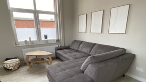 Ein modernes Wohnzimmer mit einem grauen Ecksofa, einem Holztisch und einem Korbwäschesack.