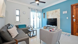 A living room with a sofa, armchair, TV, ceiling fan, and a door with a sign.