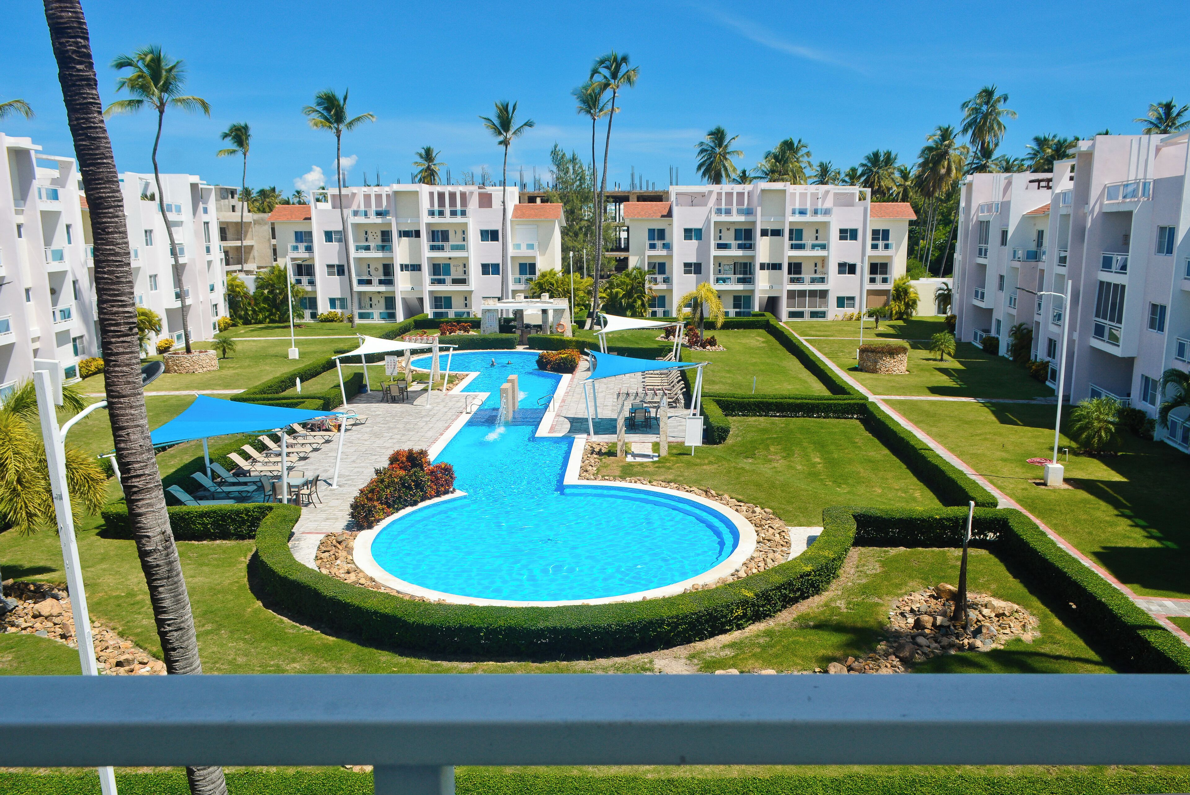 Un complexe hôtelier doté d’une piscine centrale, de nombreux balcons et de palmiers.