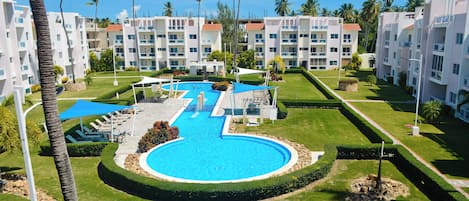 Un complexe hôtelier doté d’une piscine centrale, de nombreux balcons et de palmiers.