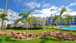 A resort with a swimming pool, palm trees, and a well-maintained lawn. - Beautiful 2-bedroom 3rd level condo with private rooftop terrace  (Punta Cana)