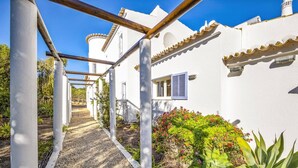 A pathway leading to a white building with a window and a door, surrounded by plants and a clear blue sky. - Villa Quinta Marta Luisa by Villa Plus (Silves)