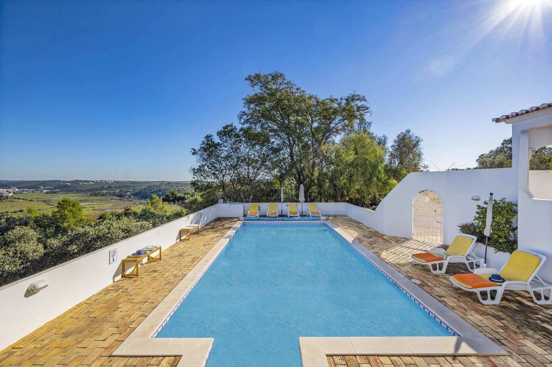 A rectangular pool with a clear blue water surface, surrounded by a white wall and a wooden deck.