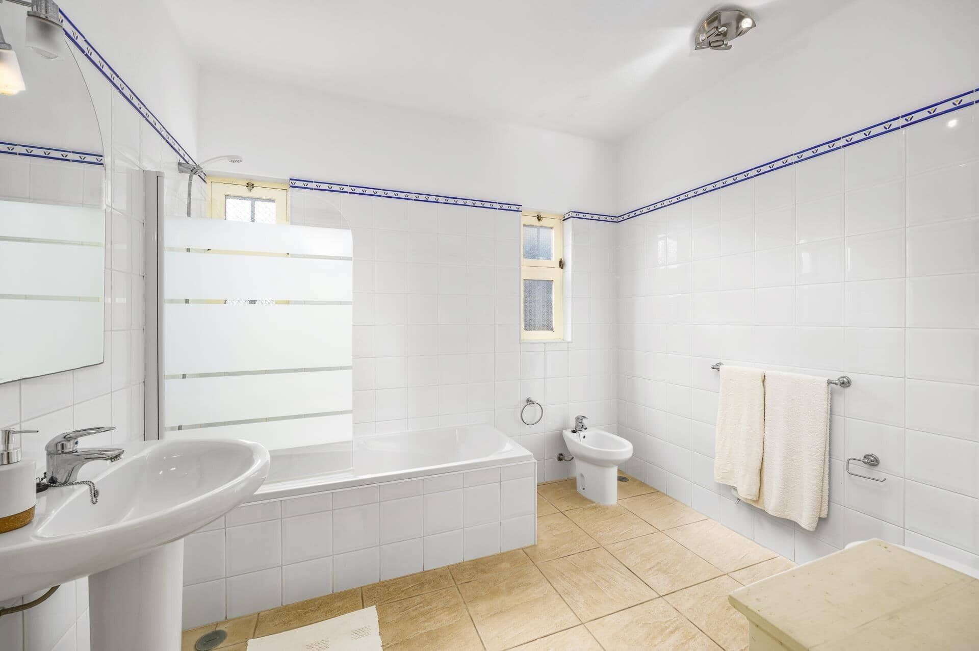 Une salle de bain moderne avec des carreaux blancs, une baignoire, un lavabo, des toilettes et une fenêtre.
