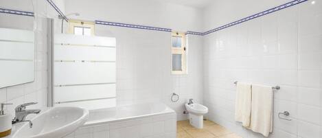 Une salle de bain moderne avec des carreaux blancs, une baignoire, un lavabo, des toilettes et une fenêtre.