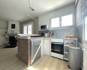 A modern kitchen with a brick fireplace, stainless steel appliances, and a window with curtains.