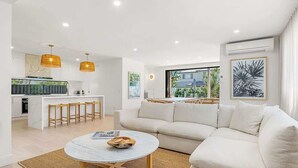 Una sala de estar moderna con un sofá, una mesa redonda de centro y una zona de cocina al fondo.