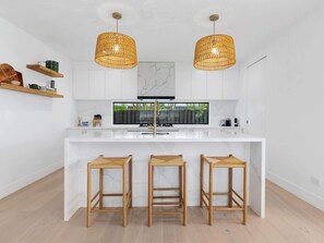 A modern kitchen with white cabinetry, a central island with stools, and two hanging wicker pendant lights.
