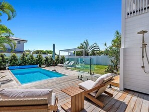 A swimming pool with lounge chairs, a wooden deck, and a glass fence.