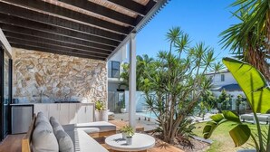 Un espacio exterior moderno con pared de piedra, terraza de madera y piscina al fondo.