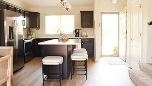 Una cocina moderna con una isla central, taburetes de bar, electrodomésticos de acero inoxidable y vistas al exterior.