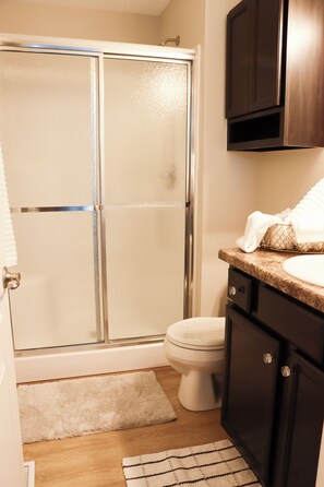 A bathroom with a glass shower door, a toilet, a sink, and dark wooden cabinets.
