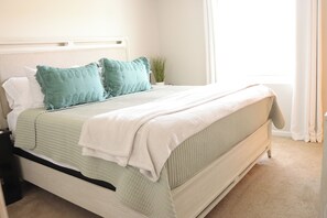 A neatly made bed with a white headboard, green and white bedding, and a small potted plant beside it.