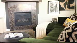 Una sala de estar con chimenea, sofá verde y una mesa de centro con un libro.