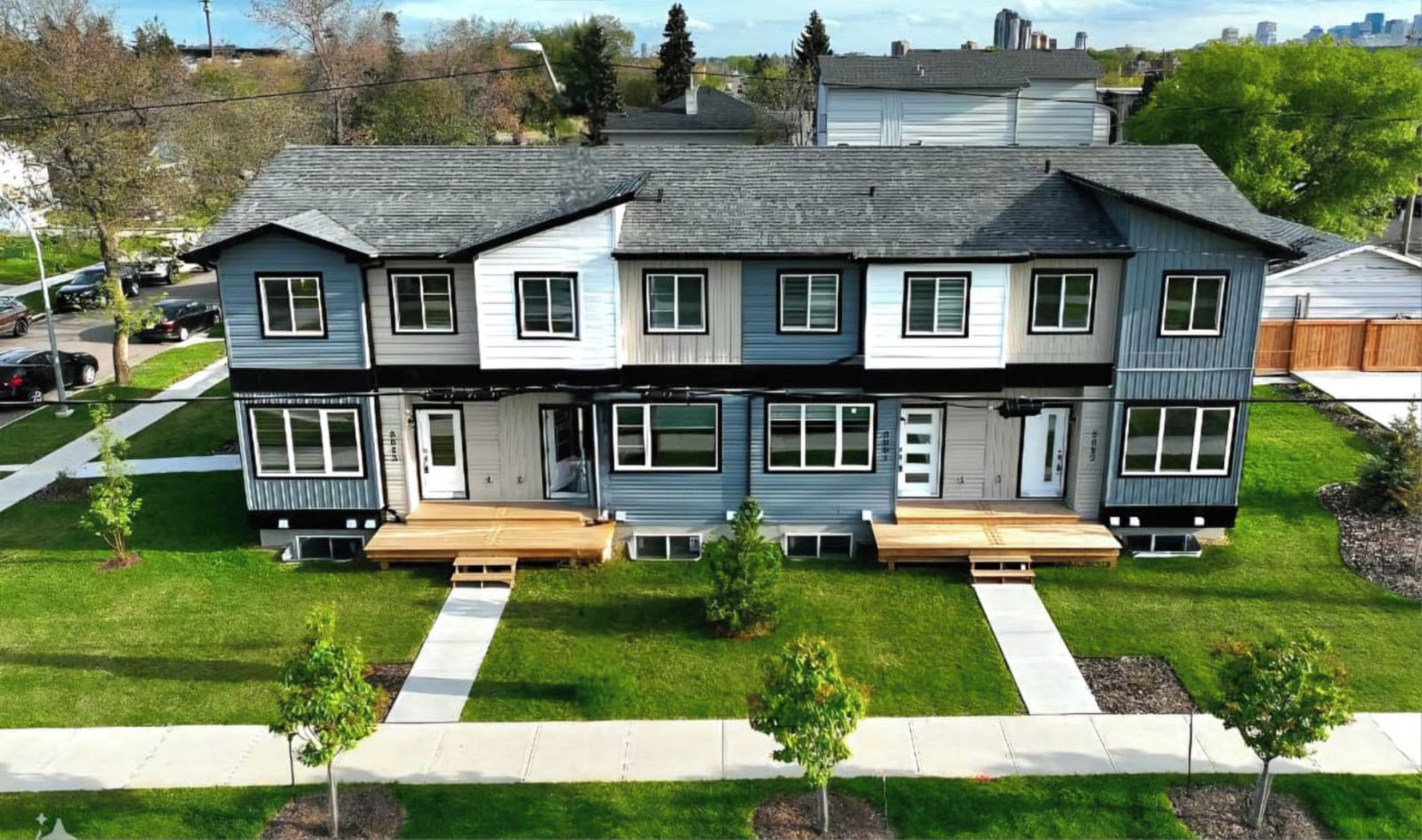 A two-story residential building with a front porch, a driveway, and a well-maintained lawn with small trees.