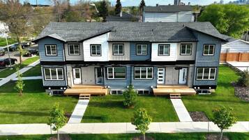 A two-story residential building with a front porch, a driveway, and a well-maintained lawn with small trees.