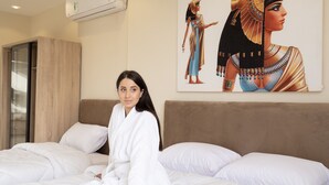 Una habitación de hotel con una cama, un aire acondicionado instalado en la pared y un cuadro grande de una figura egipcia.