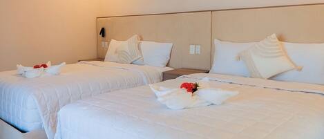 Habitación de hotel con dos camas, cada una con ropa blanca de cama y almohadas, y un aire acondicionado instalado en la pared.