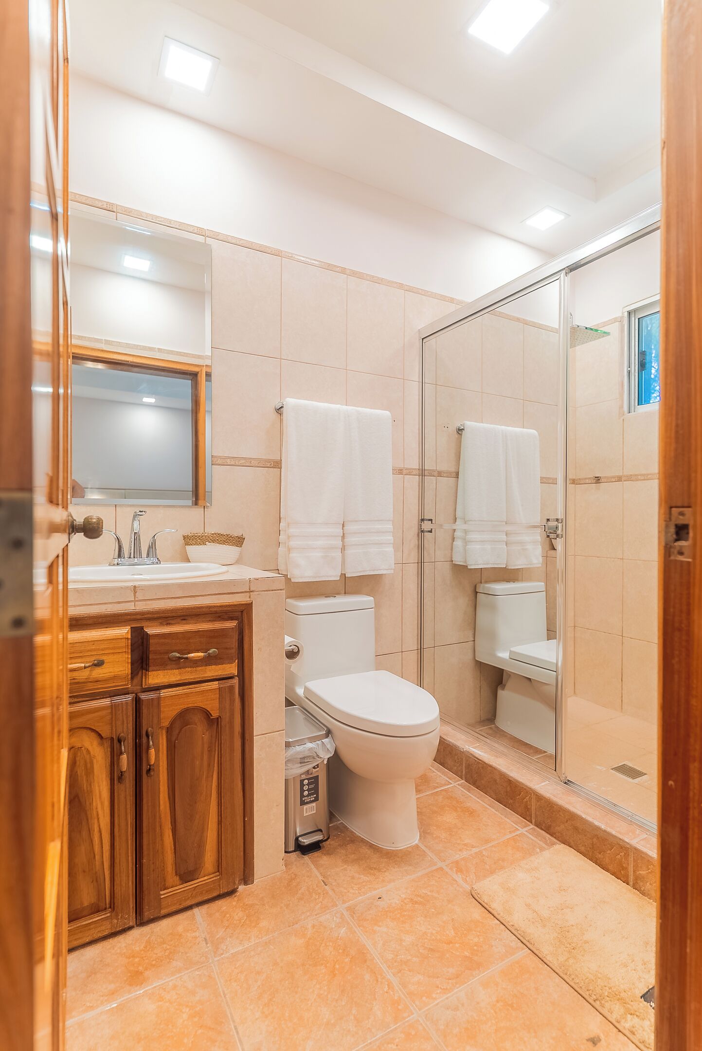 A bathroom with a wooden vanity, a toilet, a shower enclosure, and a mirror.