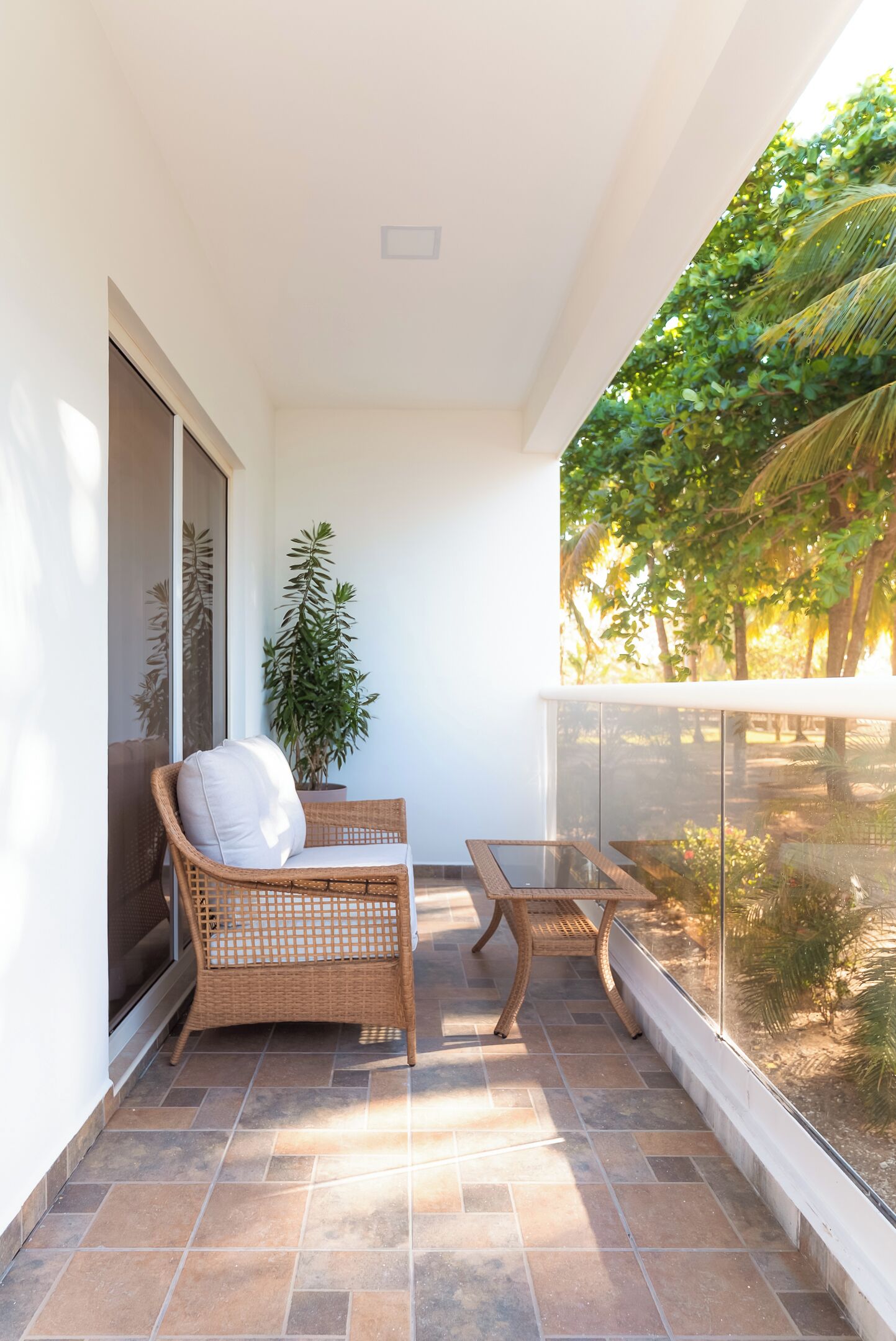 Un balcon avec un fauteuil en osier, une petite table et un pot de fleurs.