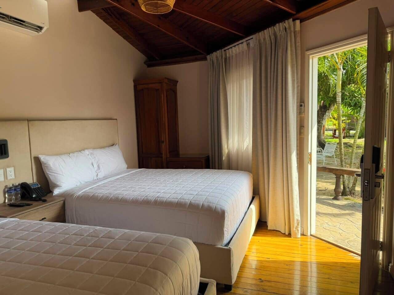 Habitación de hotel con dos camas, un armario de madera, un teléfono y vista al exterior.