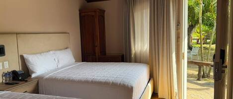 A hotel room with two beds, a wooden wardrobe, a telephone, and a view of the outdoors.