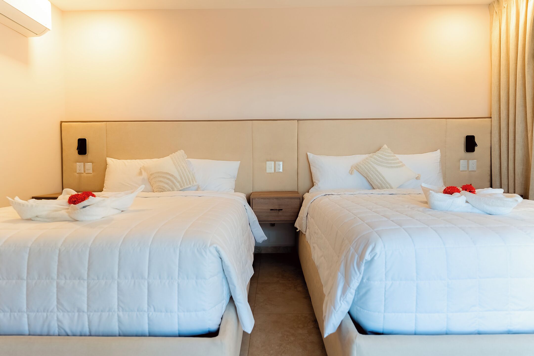 Ein Hotelzimmer mit zwei Betten, jeweils mit weißer Bettwäsche und Kissen, einem Nachttisch und einem an der Wand befestigten Telefon.