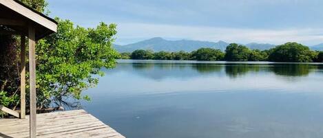 A wooden dock extending into calm water, surrounded by lush greenery and distant mountains.