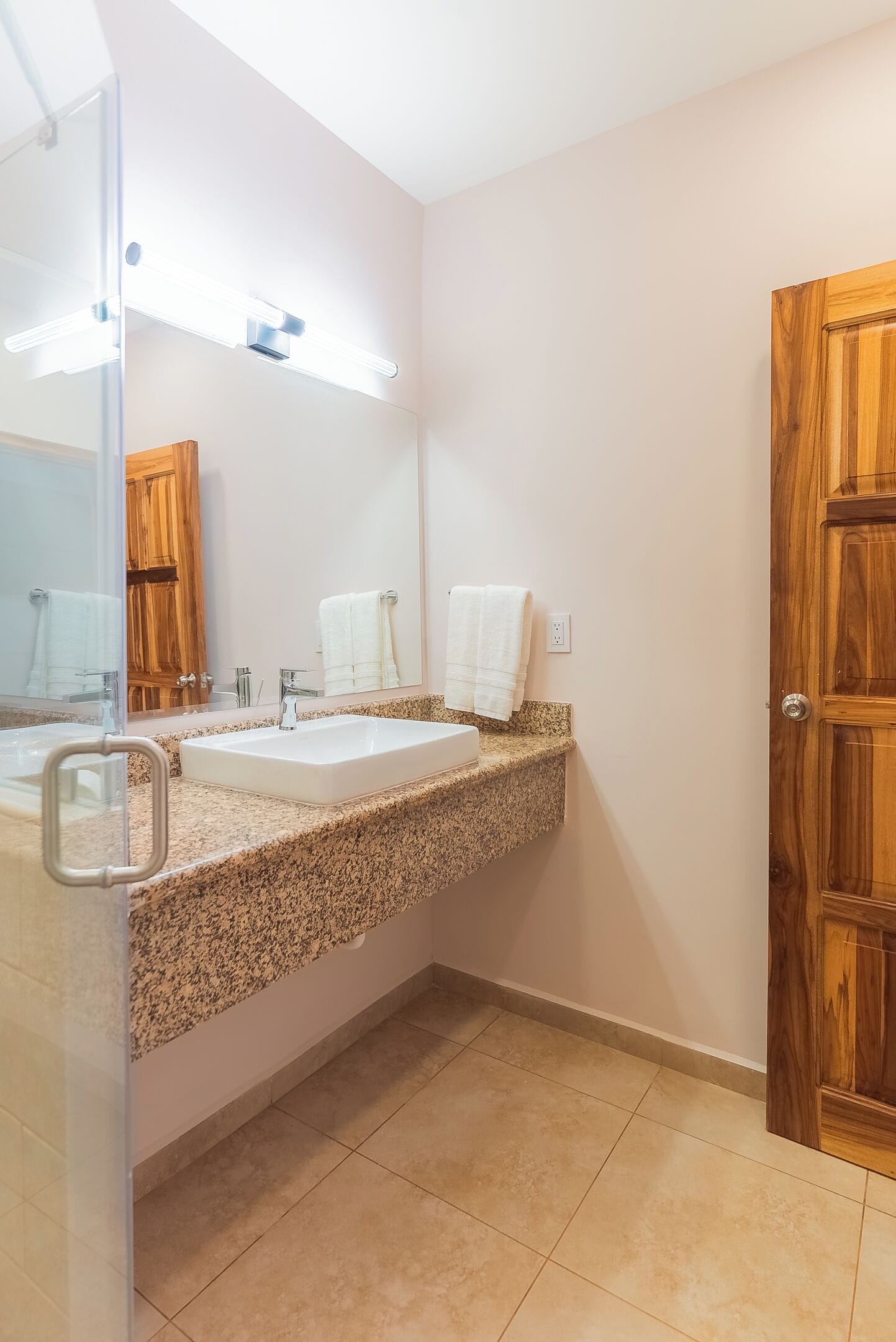Baño con dos lavamanos, un espejo y una puerta de madera.
