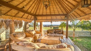 A thatched-roof gazebo with wicker furniture and a view of a landscaped garden.