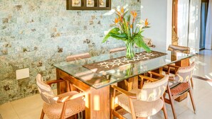 A dining area with a glass-top table, wooden chairs, and a vase with flowers.