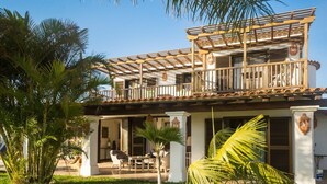 A two-story building with a covered patio area, outdoor seating, and palm trees.