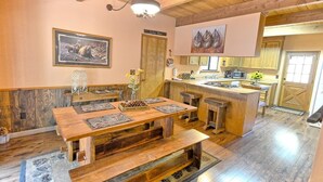 A rustic cabin interior with a wooden dining table, benches, a kitchen area, and a framed wildlife painting. - Cozy 3-bedroom cabin in superb Arnold with WiFi and a Spa (Arnold)
