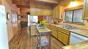 A kitchen with wooden cabinets, a central island, and a window overlooking a garden. - Cozy 3-bedroom cabin in superb Arnold with WiFi and a Spa (Arnold)
