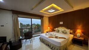 Una habitación de hotel con una cama grande, un balcón con vistas, una mesita y una silla.