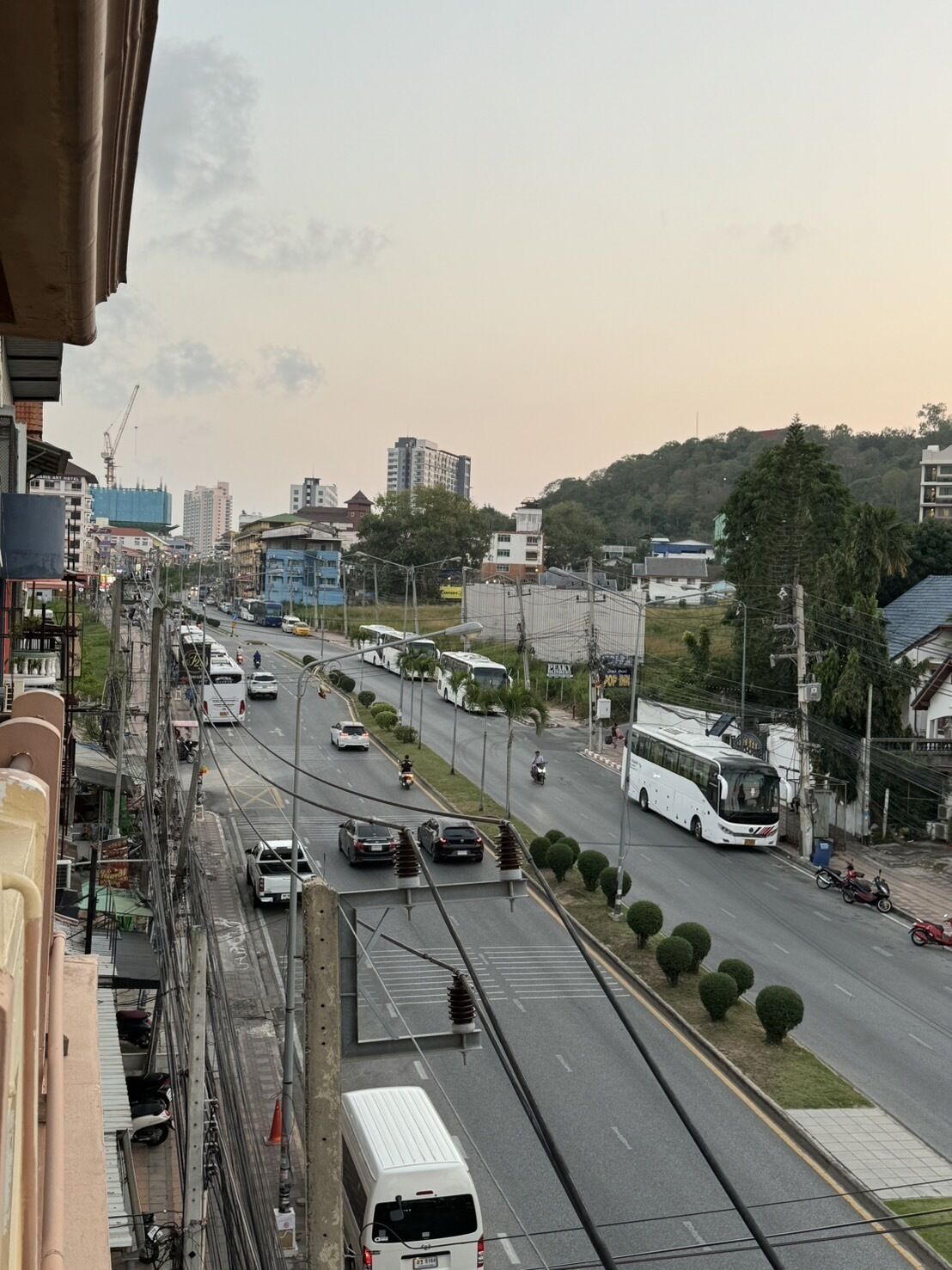Egy több sávos út, amelyen különféle járművek közlekednek, köztük személyautók, motorkerékpárok és buszok. Az út mindkét oldalán épületek találhatók, és a távolban egy építési daru is látható.