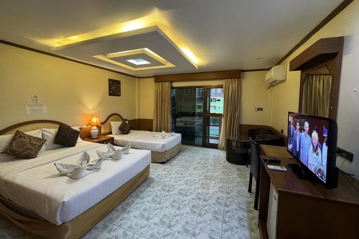 A hotel room with two beds, a desk with a TV, and a balcony with curtains.