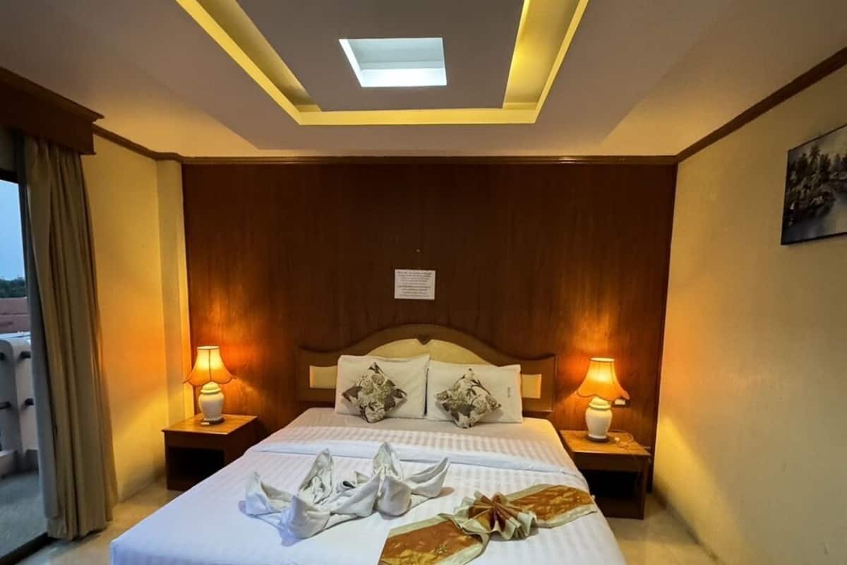 A hotel room with a large bed, two bedside lamps, a ceiling light, and a view of the outdoors.