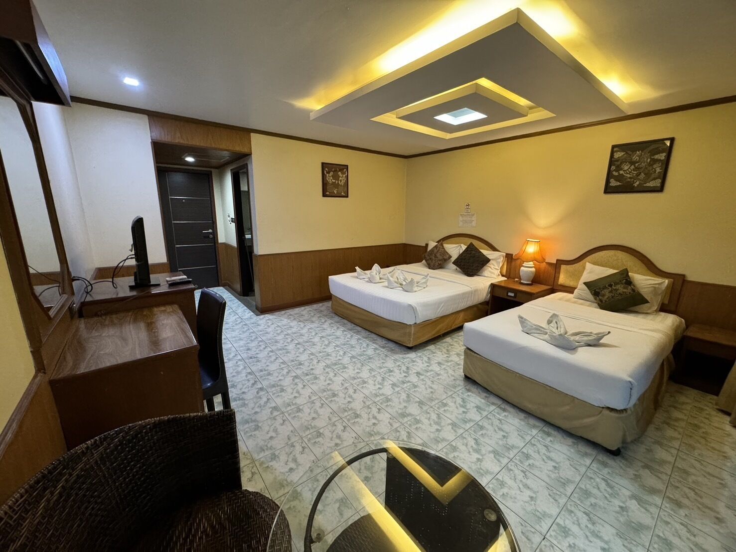 A hotel room with two beds, a desk, a chair, and a ceiling light fixture.