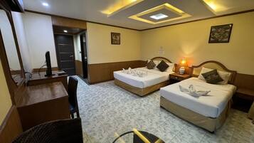 A hotel room with two beds, a desk, a chair, and a ceiling light fixture.