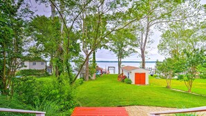 A red wooden pathway leading to a small building with a red door, surrounded by lush greenery and trees, with a body of water in the background. - WATERFRONT!!! The River's Roost on The Patuxent River (Saint Leonard)