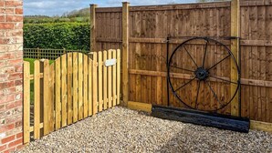 Un cancello di legno con un cartello, una carriola e un vialetto sterrato che conduce a un muro in mattoni.
