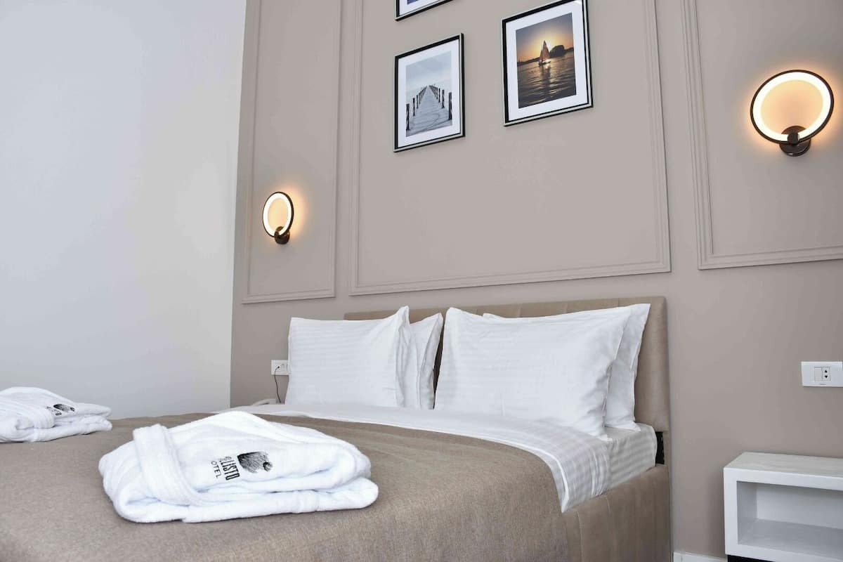 A hotel room with a bed, white linens, a folded robe, and wall-mounted light fixtures.
