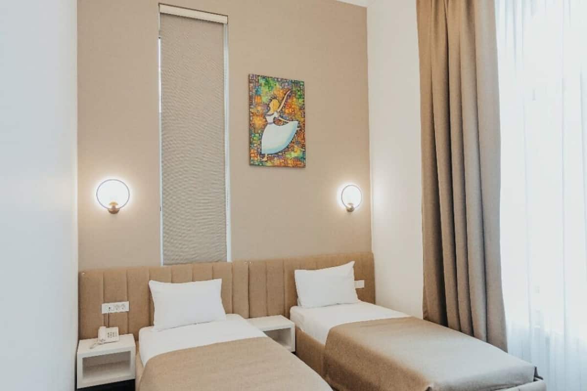 A hotel room with two beds, a painting on the wall, and a window with curtains.