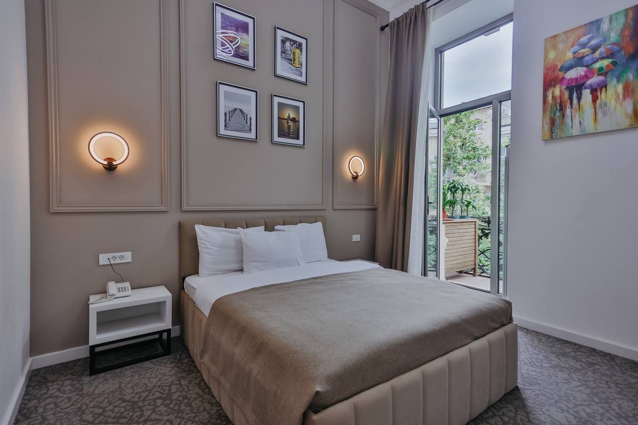A bedroom with a bed, bedside table, wall-mounted light, and a window with a view.