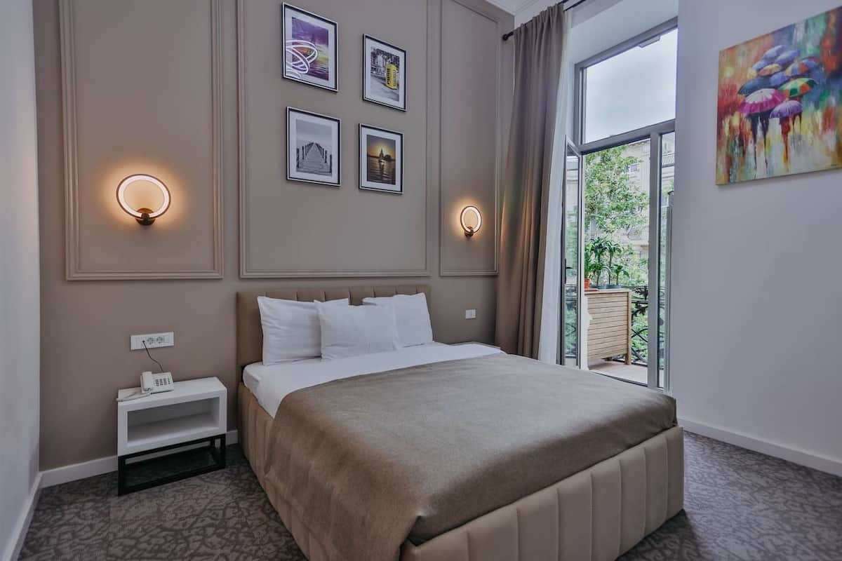 A bedroom with a bed, bedside table, wall-mounted light, and a window with a view.