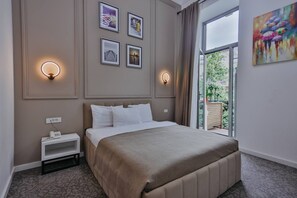 A bedroom with a bed, bedside table, wall-mounted light, and a window with a view.